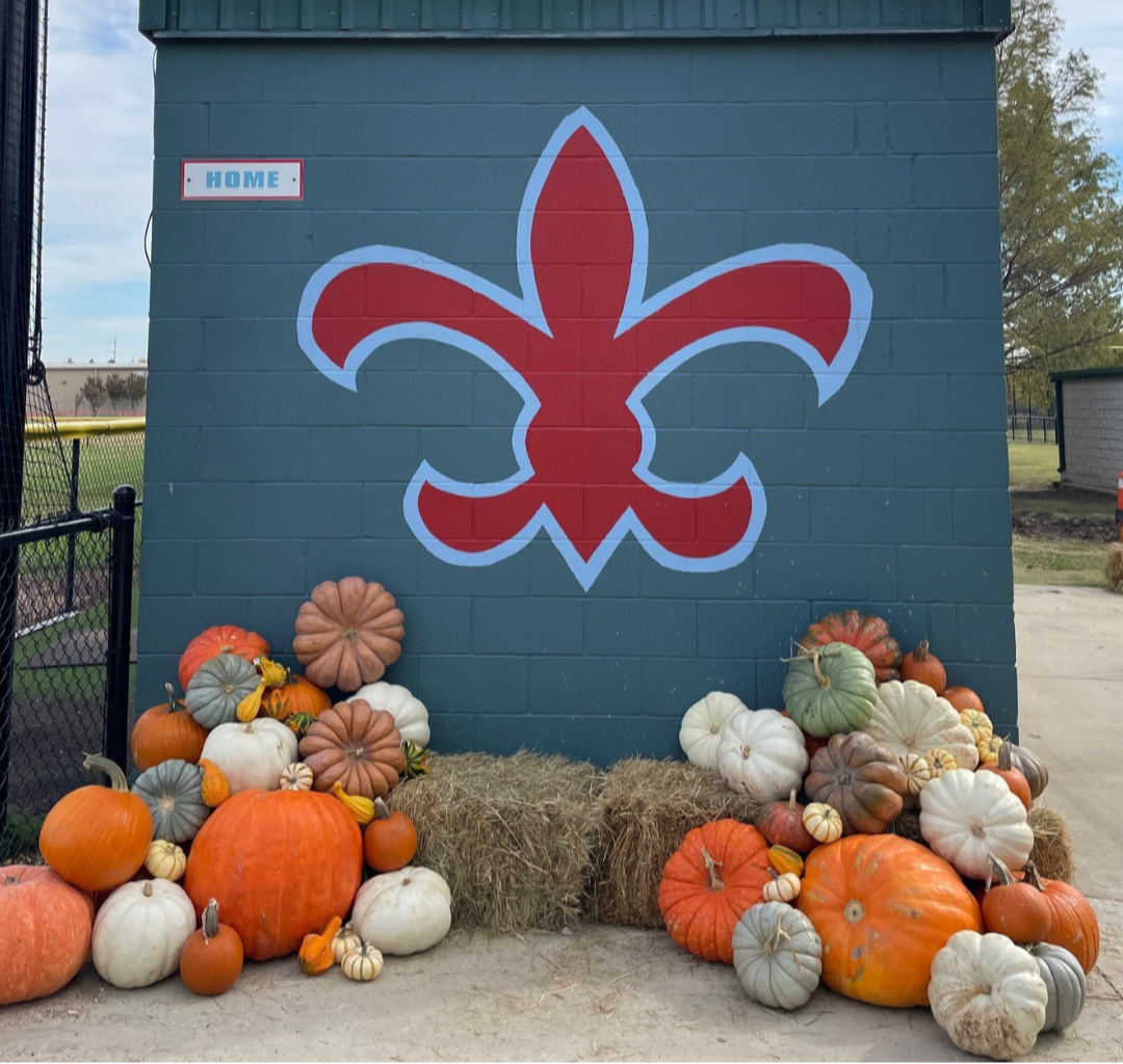 Blue wall with red and white fleur-de-lis design, surrounded by pumpkins and hay bales.