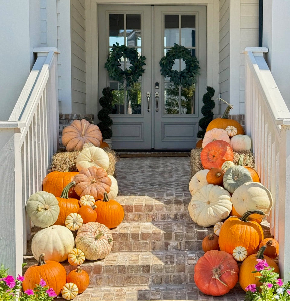 Decorative display of pumpkins on a staircase leading to a front door with wreaths.