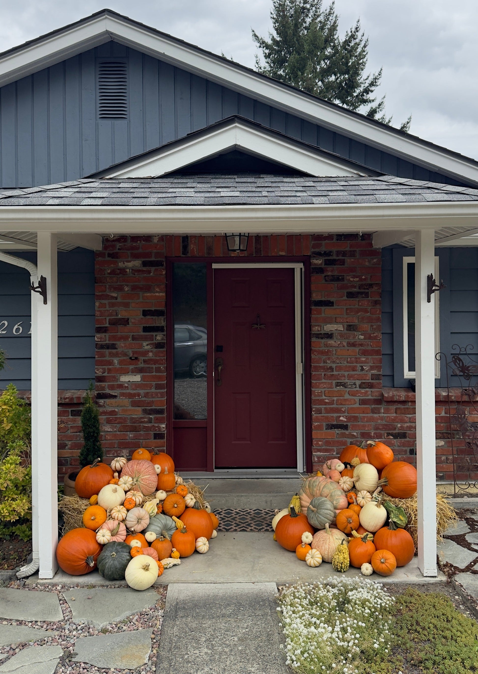 Decorative pumpkins in front of a house with a gray roof and white columns.