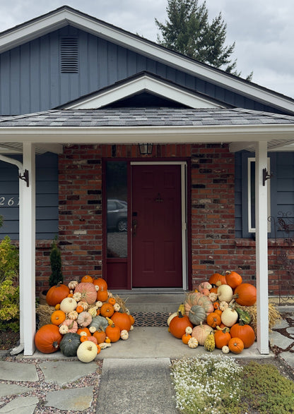 Decorative pumpkins in front of a house with a gray roof and white columns.