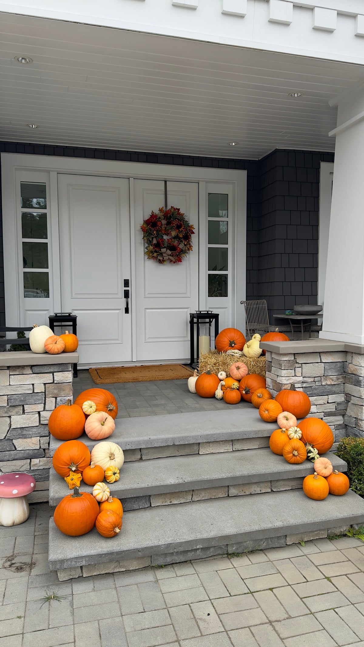Outdoor front porch decorated with multiple orange and white pumpkins, a fall wreath, and a small duck ornament on stone steps.