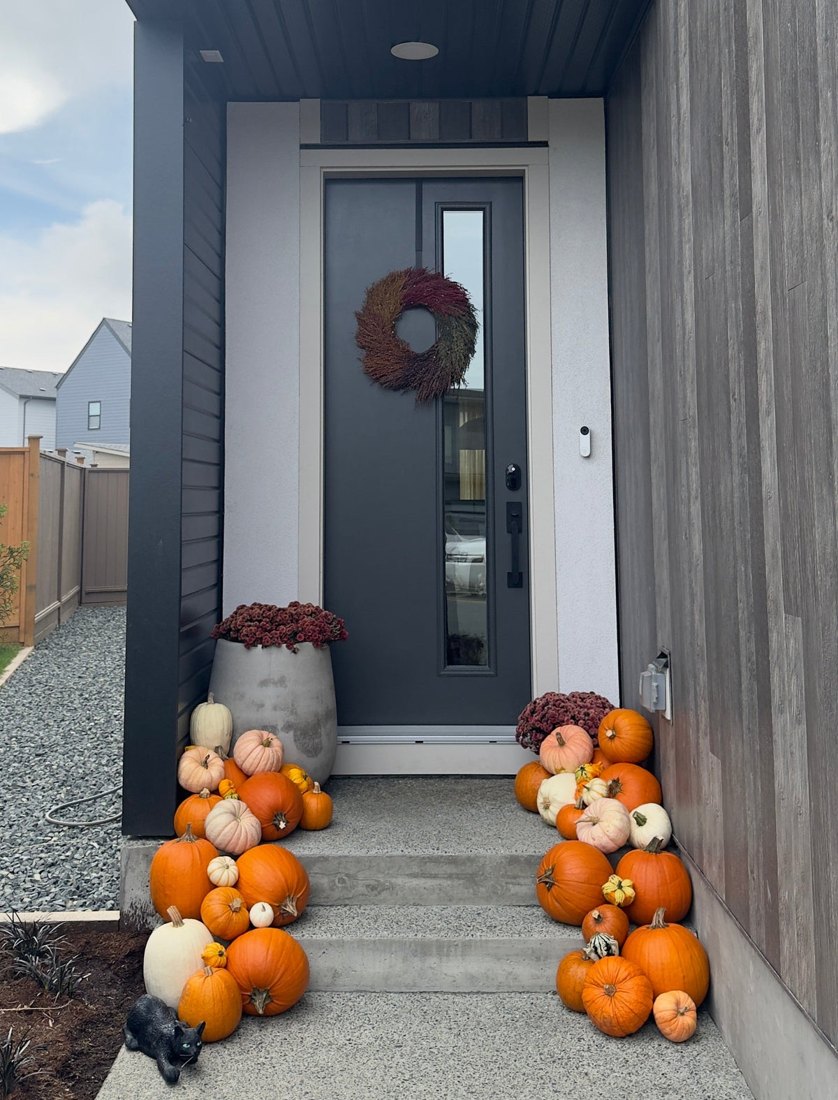 A modern house front porch decorated with numerous orange and white pumpkins arranged on the steps and beside the dark gray front door, which has a round wreath hanging on it.