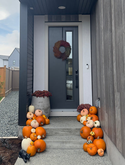 A modern house front porch decorated with numerous orange and white pumpkins arranged on the steps and beside the dark gray front door, which has a round wreath hanging on it.