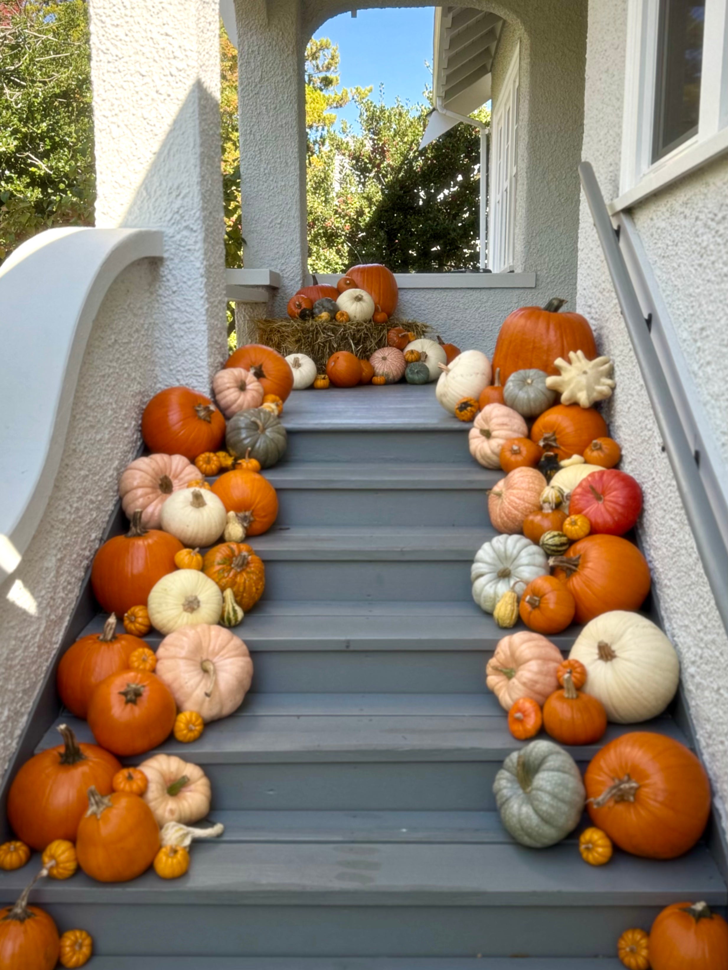 Gray outdoor staircase decorated with an abundance of orange, beige, and white pumpkins and gourds, set against a white stucco house exterior.