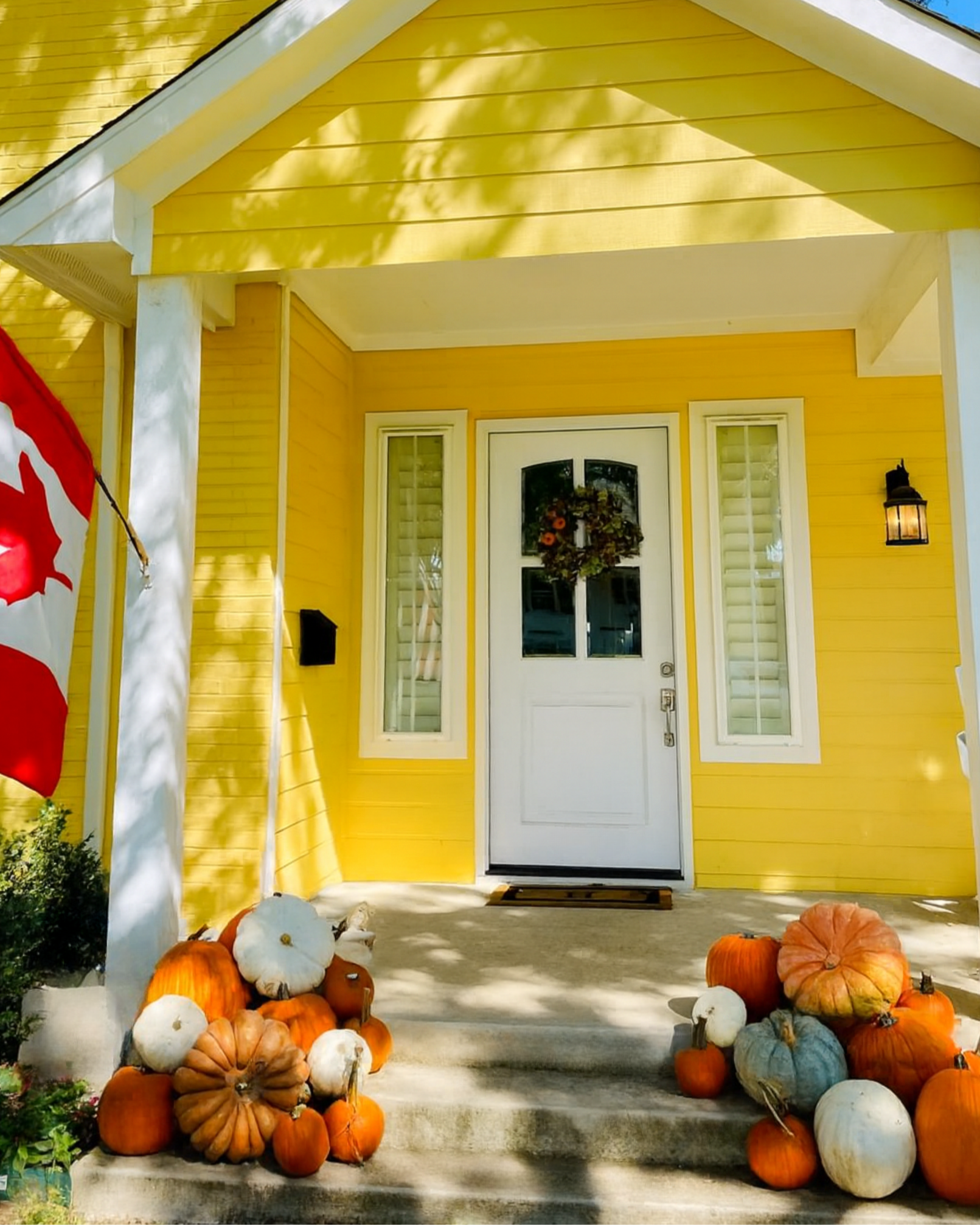 Assorted pumpkins decorate the porch of a yellow house.